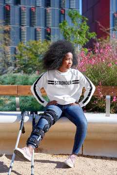 Black woman in leg brace sitting on bench in city