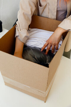 Crop unrecognizable woman unpacking box with clothes