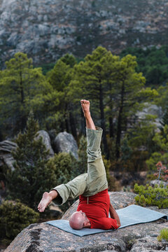 Middle aged man doing Shoulder Stand in mountains 
