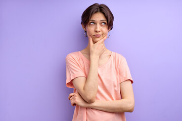 Obraz premium young woman thinking, in contemplation touching chin, concentrated on thoughts, wearing casual outfit. isolated purple background