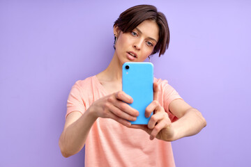 Female model making doing selfie on mobile phone, blogging. Good-looking female with short hair looks at phone's camera and posing, wearing casual outfit
