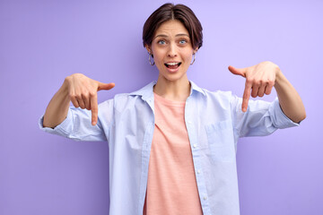 Cheerful woman with short hair pointing index finger down, showing. copy space, free space for...