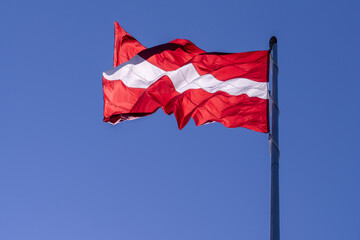 Fototapeta na wymiar The flag of Latvia waving in the wind against the skylight of the sun on a background of the sky