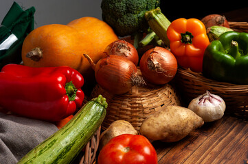 Still life of fresh vegetables on wooden table with wicker baskets, squash, bell peppers, broccoli.