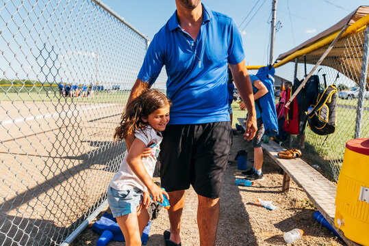 Father carrying daughter through baseball dugout. 