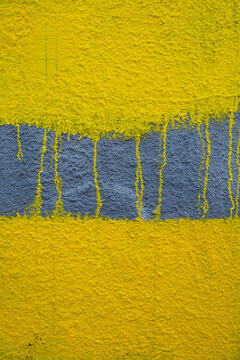 Dripping yellow paint covering graffiti on building wall, close up