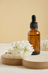 brown bottle with a dropper for cosmetic oils or serums and a branch of white lilac on a beige background