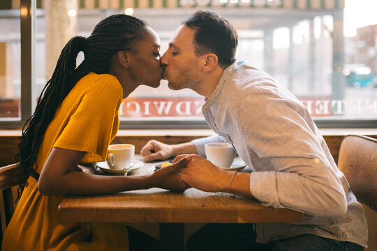 Happy diverse couple kissing during date in cafe