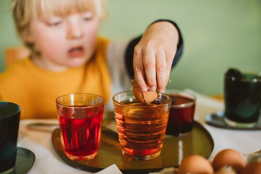 A toddler stirs easter eggs in orrange dye