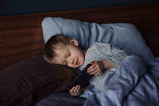 Little boy using phone in bed