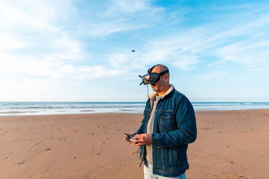 Man Controlling Drone Flying Over Beach At Sunset 