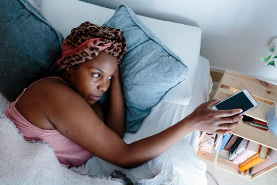 Woman In Bed Grabbing Her Cell Phone From Night Table In The Morning