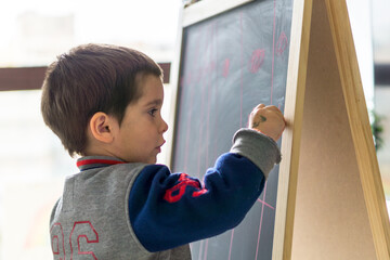 Kid writing with chalk on a blackboard in his living room