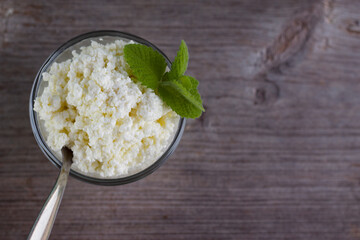 Cottage cheese in a bowl with mint on the wooden table. Fresh curd with top view. Healthy breakfast concept. 
