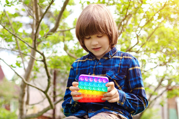 Сhild playing with antistress toy pop it. A joyful boy is holding and push a trendy popular finger toy. Kid trains motor skills. ..Rainbow silicone bubble play. Brighter modern entertainment