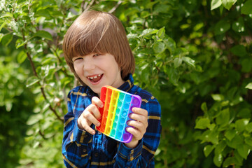 Сhild playing with antistress toy pop it. A joyful boy is holding and push a trendy popular finger toy. Kid trains motor skills. ..Rainbow silicone bubble play. Brighter modern entertainment