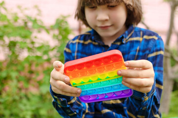 Сhild playing with antistress toy pop it. A joyful boy is holding and push a trendy popular finger toy. Kid trains motor skills. ..Rainbow silicone bubble play. Brighter modern entertainment