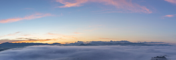 Fototapeta na wymiar Panoramic beautiful misty morning mountain peaks with orange blue gradient of dawn sky.