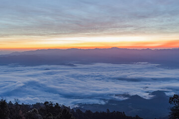 Mountain peaks in morning fog - foggy with orange blue gradient of dawn sky.