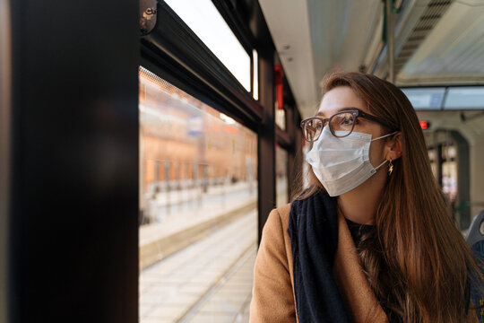 Young woman in mask looking out train window