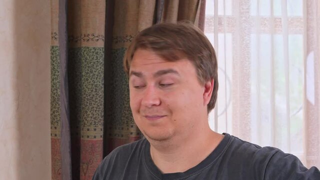 Young Caucasian man smiles and nods his head playfully, making a suggestive gesture with eyebrows, plotting a prank, front view. Portrait of flirting guy.