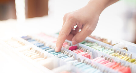 Close up hands of tailor woman choosing ocean blue threads and different colors in the box put on the table and prepare to use with white cotton and frame wood.