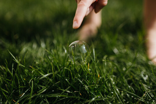 finger pointing to soap bubble in the grass