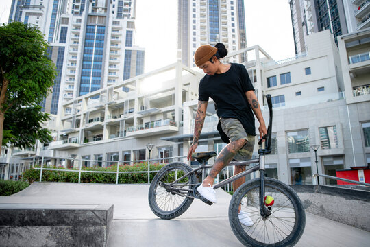 Portrait of a Young Tattooed man in black shirt with beanie checking his BMX.