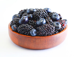 Blackberries and blueberries in a wooden bowl on a white background.