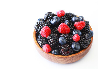 Raspberries, blackberries and blueberries in a wooden bowl on a white background.