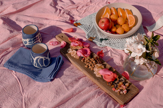 Picnic in the park with ceramic cups, lots of fruits, beautiful wooden board with nuts