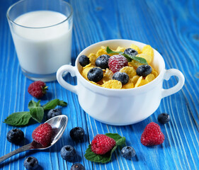 Cornflakes with berries and milk for breakfast. Blue wooden background.