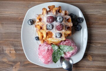 Belgian waffles with strawberry ice cream witn mint, fresh raspberries and blueberries over wooden table.