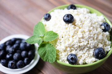 Cottage cheese with fresh blueberries in a bowl for healthy breakfast over wooden background.