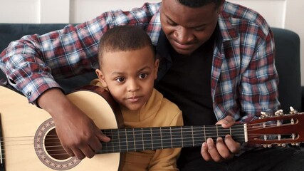 African-American man teaching his little son to play guitar at home