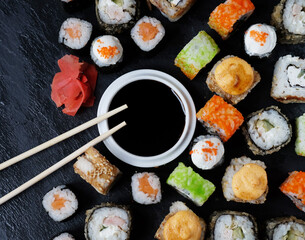 Set of sushi and maki with soy sauce and wooden sticks on stone table.