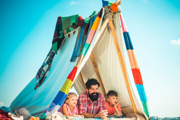 Father with kids children in tent. Summer weekend. Family playing together. Summertime vacation concept.