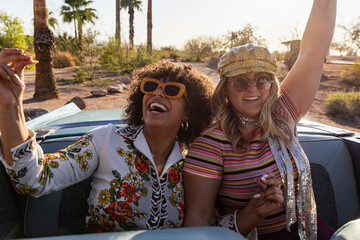 Two girls riding in back of Convertible car 