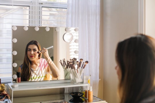 Focused woman doing makeup near mirror at home