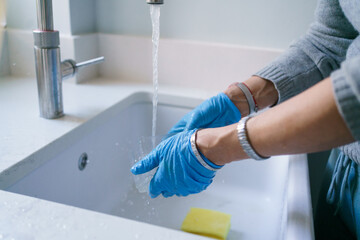 Female hands in blue rubber gloves cleaning container over modern sink