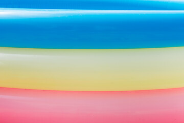 Summer: closeup of the side of blow up pool with blue, yellow, and pink rings