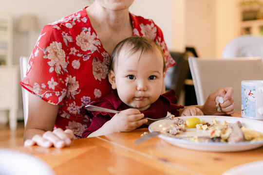 mother holding her adorable baby on her lap while eating breakfast 