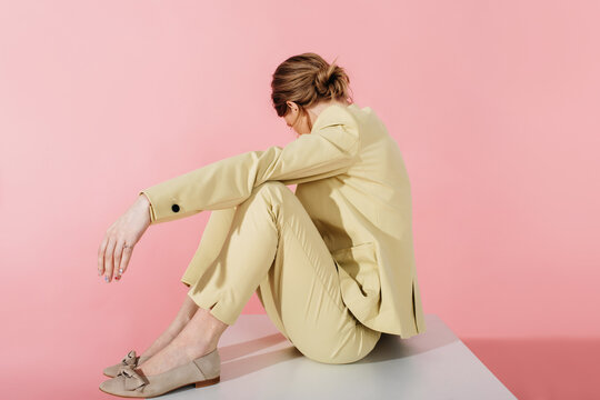 Modern woman in stylish suit sitting on cube in studio