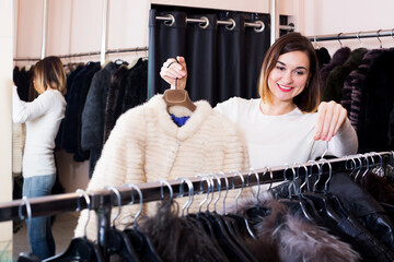 Pretty female customer examining white mink jacket in women cloths store