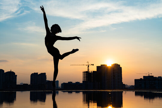 Silhouette of ballerina performing on cityscape and dramatic sunset background. Concept of willpower, control and dream