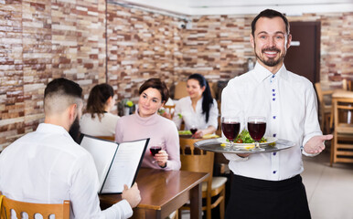 Cheerful happy waiter serving a rural restaurant guests at table