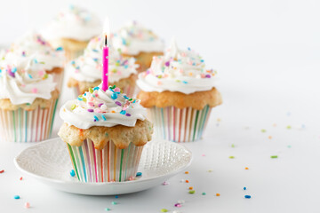 Close up of a cupcake and a lit candle with other cupcakes in soft focus in behind and copy space to the right.