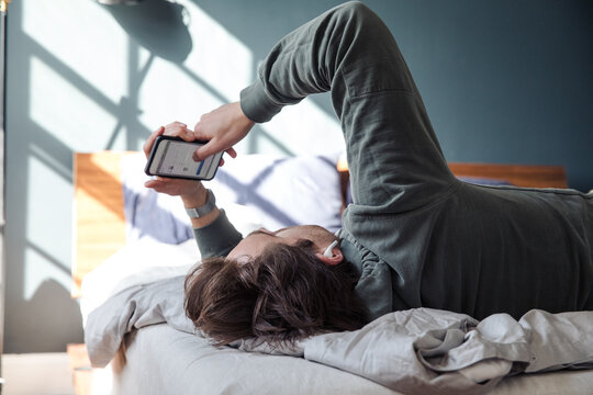 Man looks at his phone wearing headphones in bed