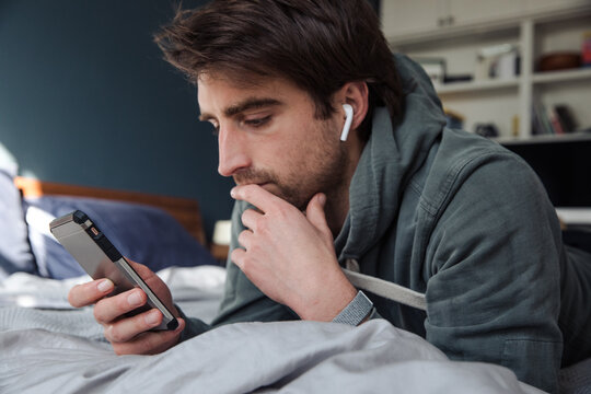 Man looks at his phone wearing headphones in bed