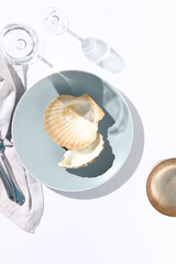 Oyster shell on blue dish. Crystal white tablecloth with glass of water, gray napkin, fork and...